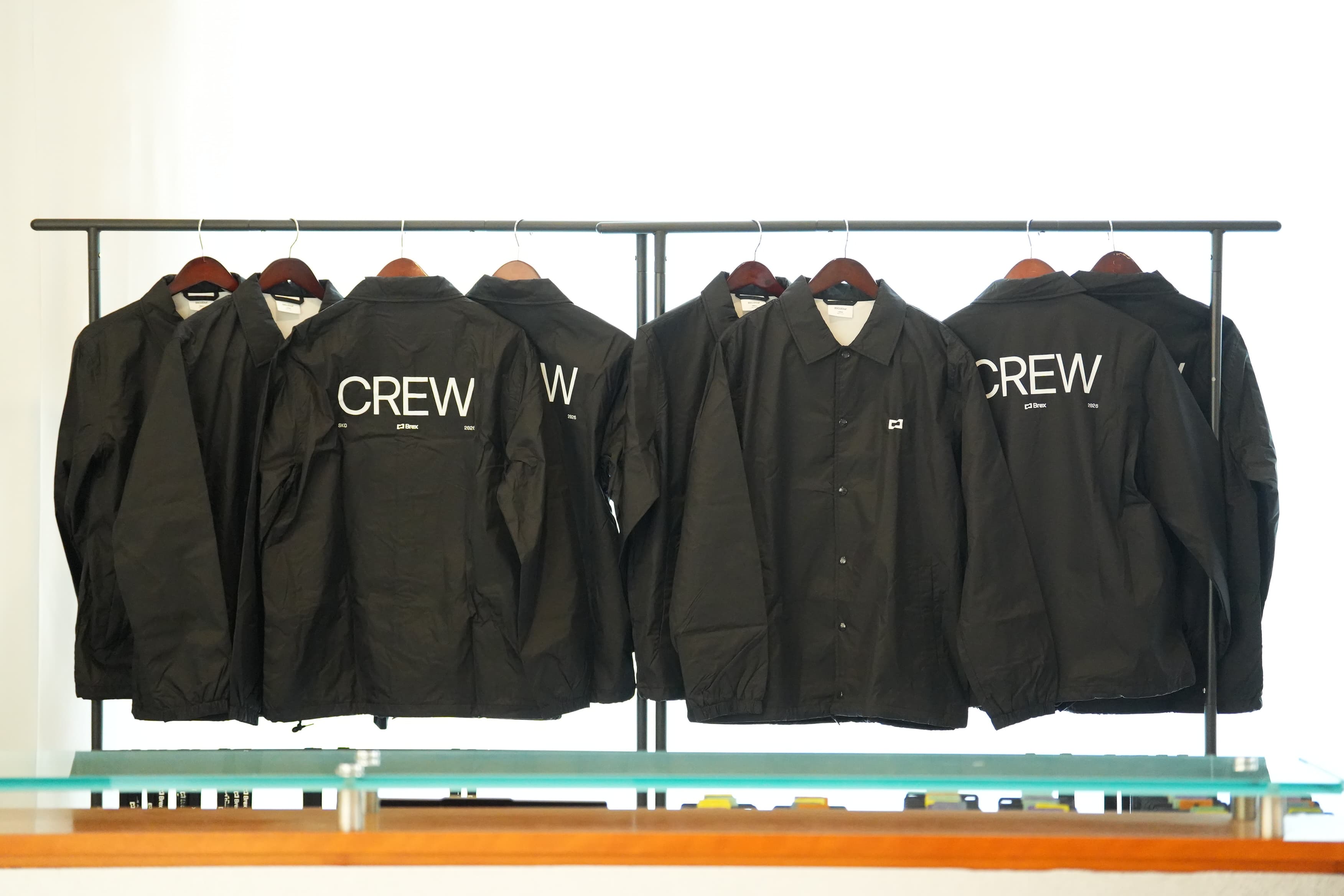 Custom black Brex CREW coach jackets displayed on a garment rack.